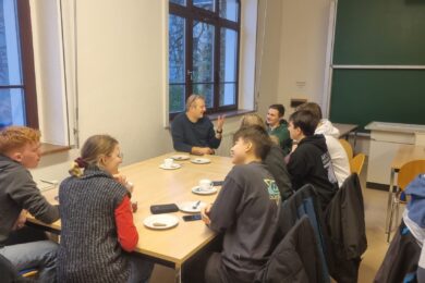 Professorenkaffeetrinken 2024, Erstis unterhalten sich bei einem Stück Kuchen mit Prof. Pfleging