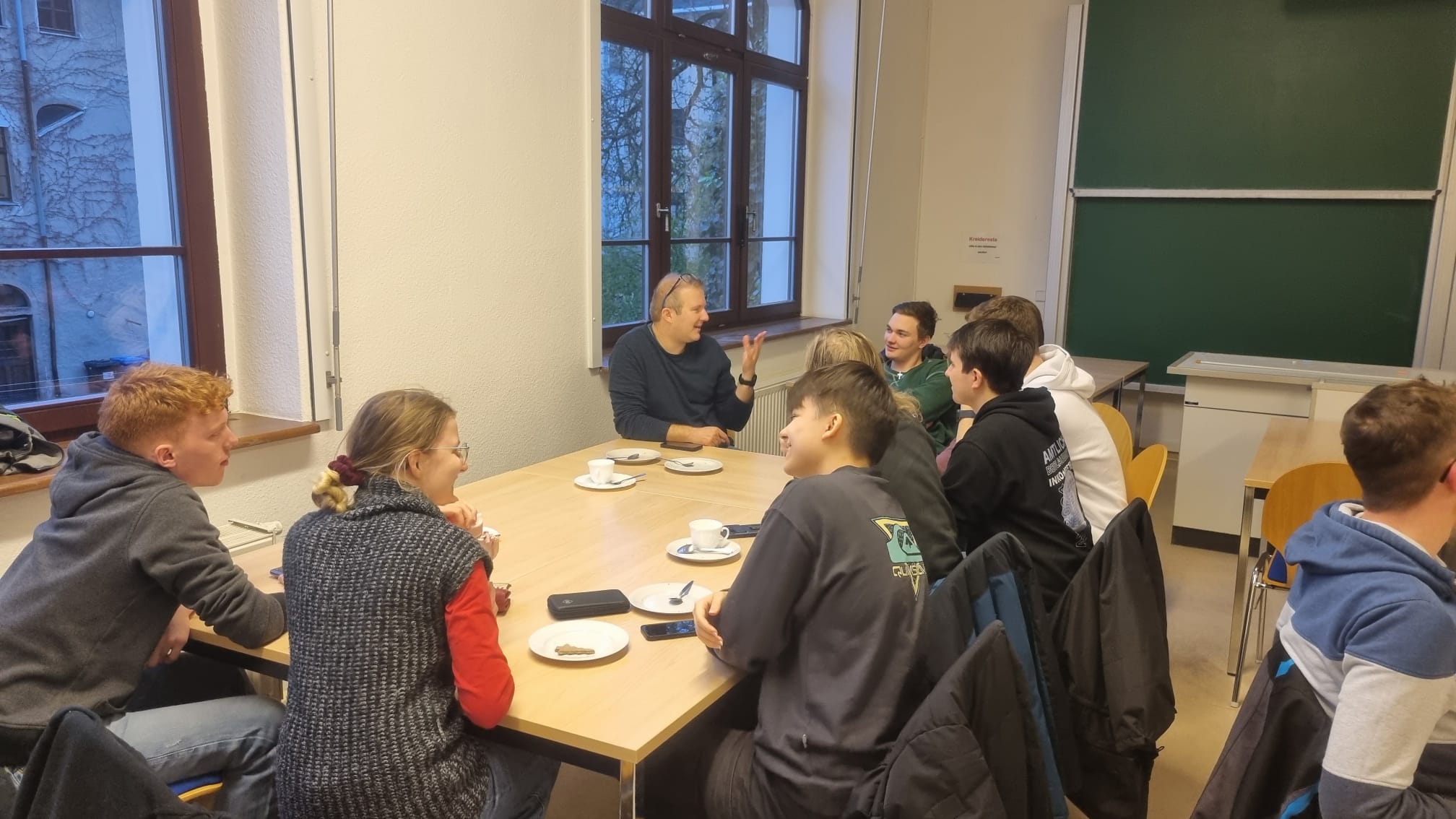 Professorenkaffeetrinken 2024, Erstis unterhalten sich bei einem Stück Kuchen mit Prof. Pfleging